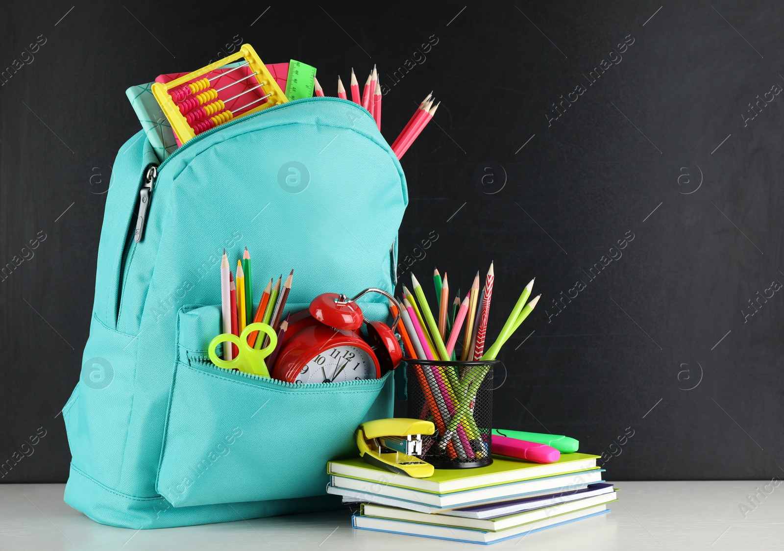 Photo of Bright backpack with school stationery on white table near black chalkboard, space for text