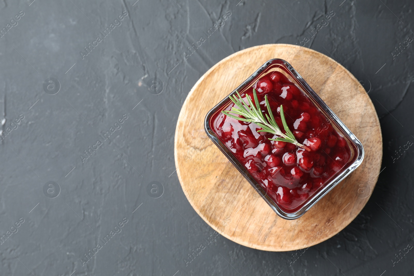 Photo of Fresh cranberry sauce and rosemary in glass bowl on gray textured table, top view. Space for text