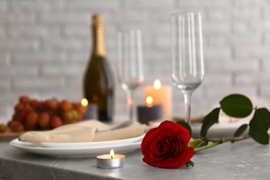 Photo of Burning candle and red rose on grey marble table indoors