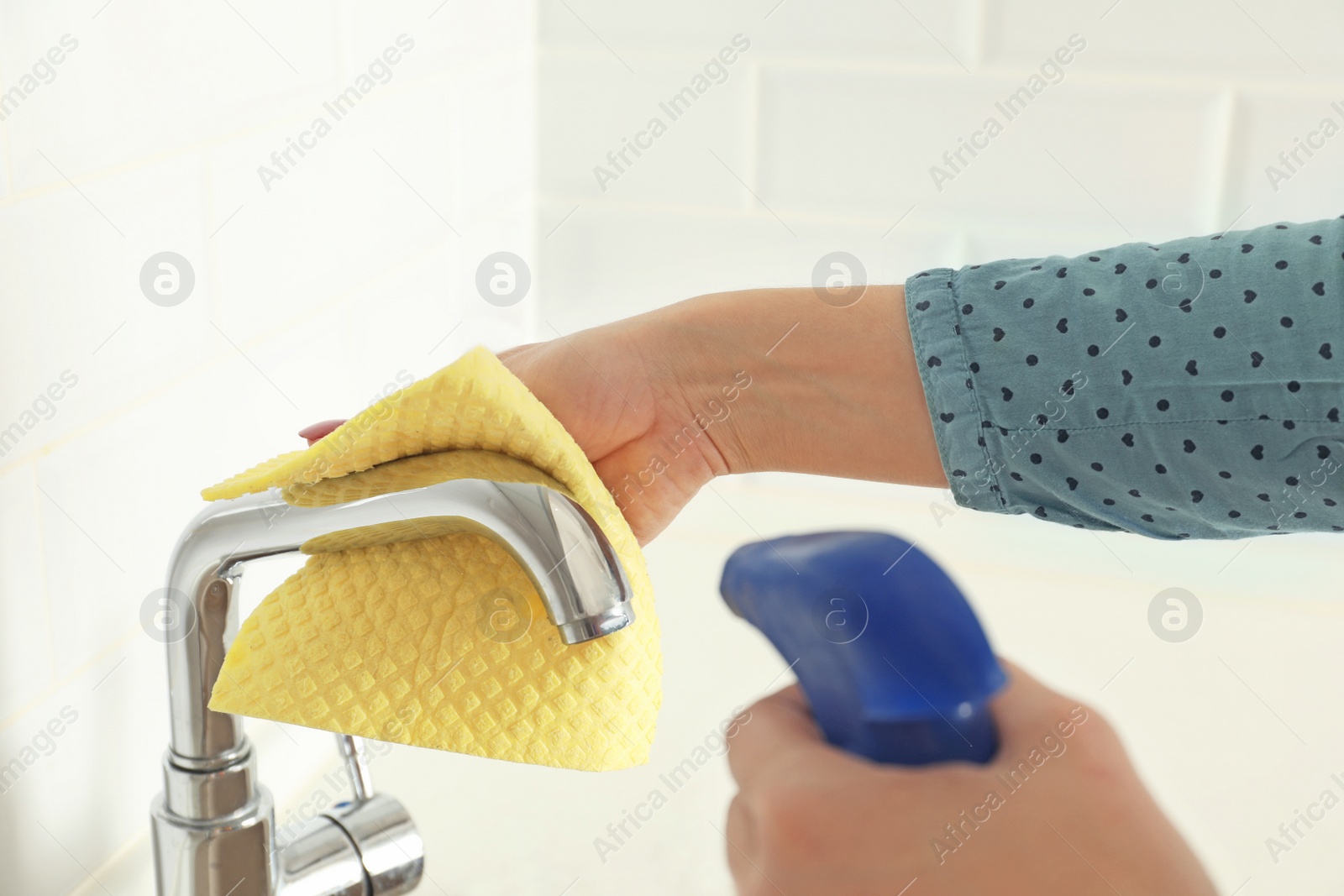 Photo of Woman cleaning tap with rag in kitchen, closeup