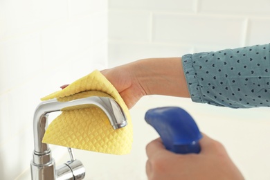 Woman cleaning tap with rag in kitchen, closeup