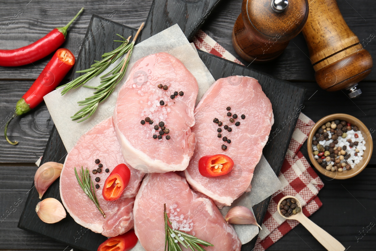 Photo of Pieces of raw pork meat, chili peppers and spices on black wooden table, flat lay