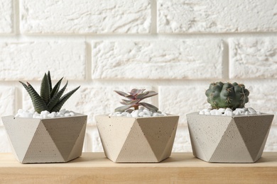 Photo of Beautiful succulent plants in stylish flowerpots on wooden table near white brick wall. Home decor