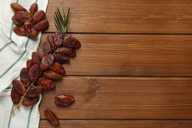 Photo of Branch with sweet dried dates and green leaf on wooden table, flat lay. Space for text