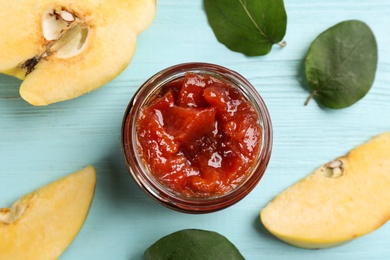 Photo of Delicious quince jam, fruits and leaves on light blue wooden table, flat lay