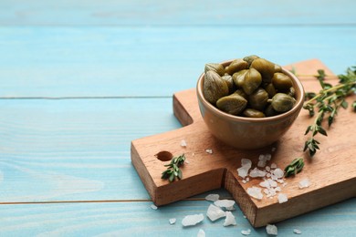 Tasty capers, thyme and salt on light blue wooden table, space for text