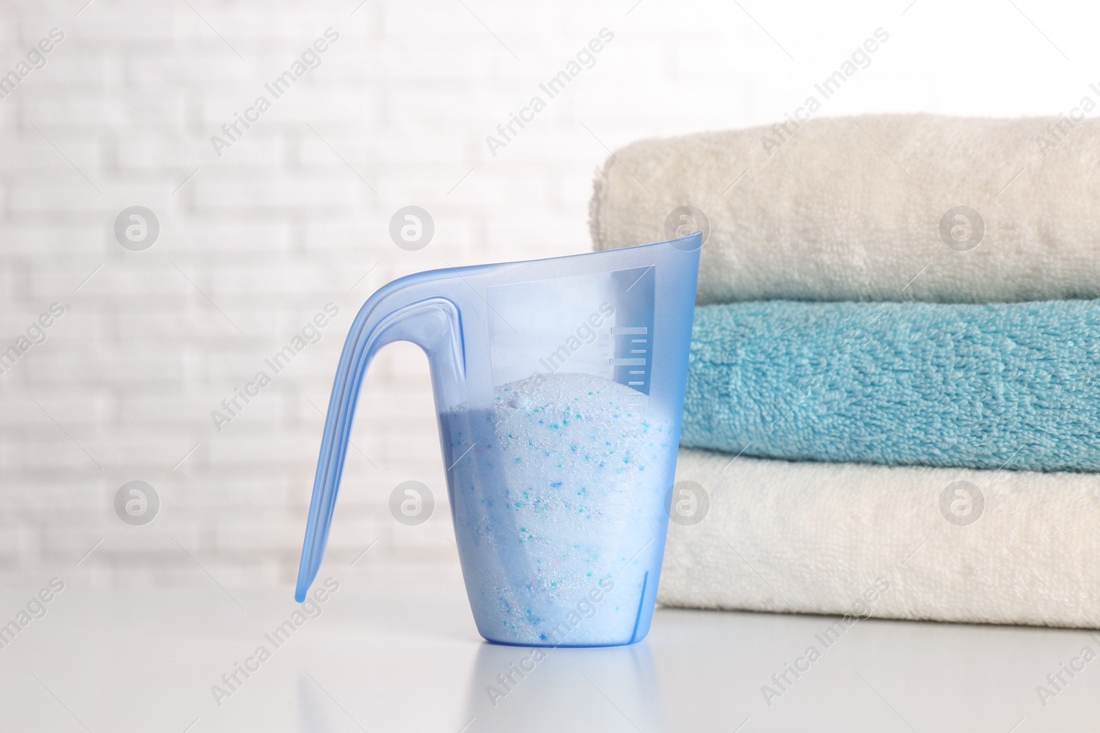 Photo of Measuring cup with washing powder and clean towels on table against brick wall. Laundry day