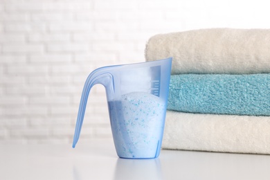 Measuring cup with washing powder and clean towels on table against brick wall. Laundry day