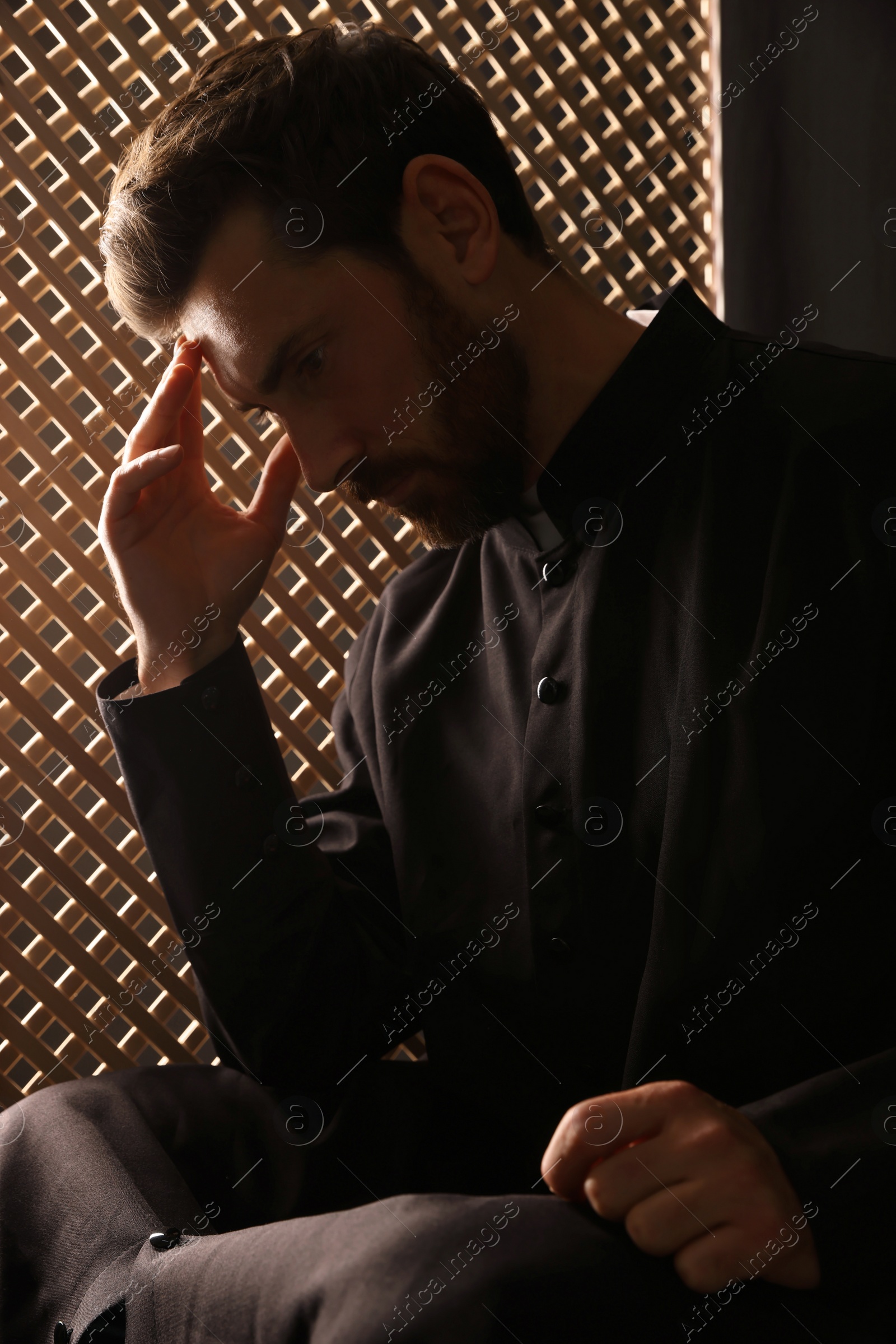 Photo of Catholic priest wearing cassock in confessional booth