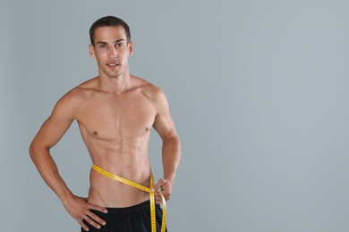 Photo of Handsome shirtless man with slim body and measuring tape around his waist on grey background. Space for text