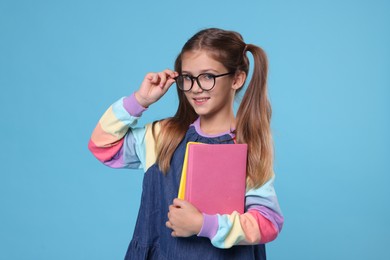 Happy schoolgirl with books on light blue background