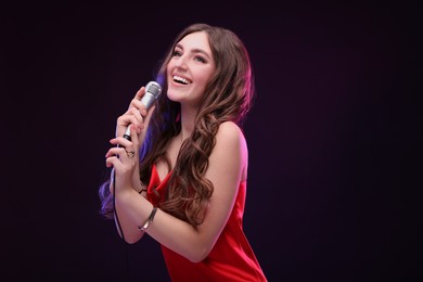 Happy woman with microphone singing in color light on black background. Space for text