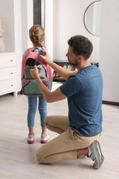 Photo of Father putting bottle of water into daughter`s backpack at home. Preparing to school