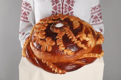 Woman with korovai on grey background, closeup. Ukrainian bread and salt welcoming tradition