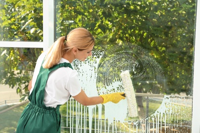 Female janitor cleaning window with squeegee indoors