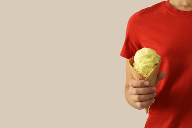 Woman holding yellow ice cream in wafer cone on light grey background, closeup. Space for text