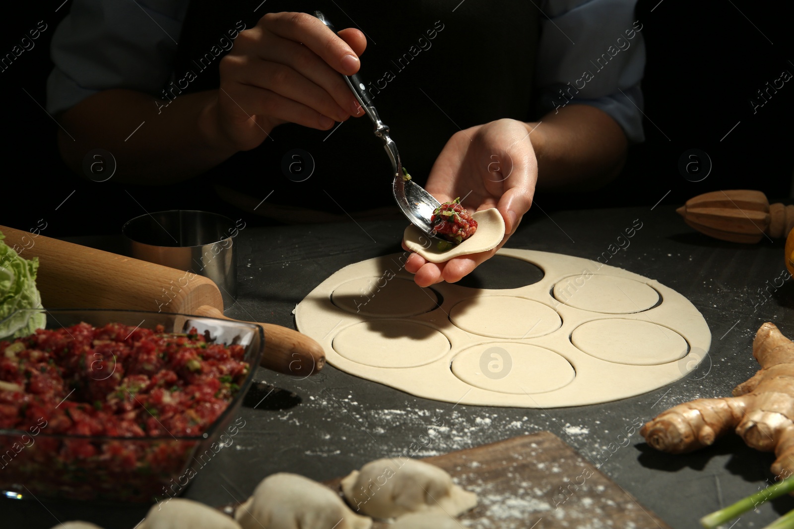 Photo of Woman putting gyoza filling in center of dough wrapper at grey table, closeup