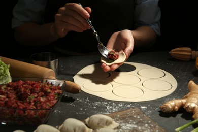 Woman putting gyoza filling in center of dough wrapper at grey table, closeup