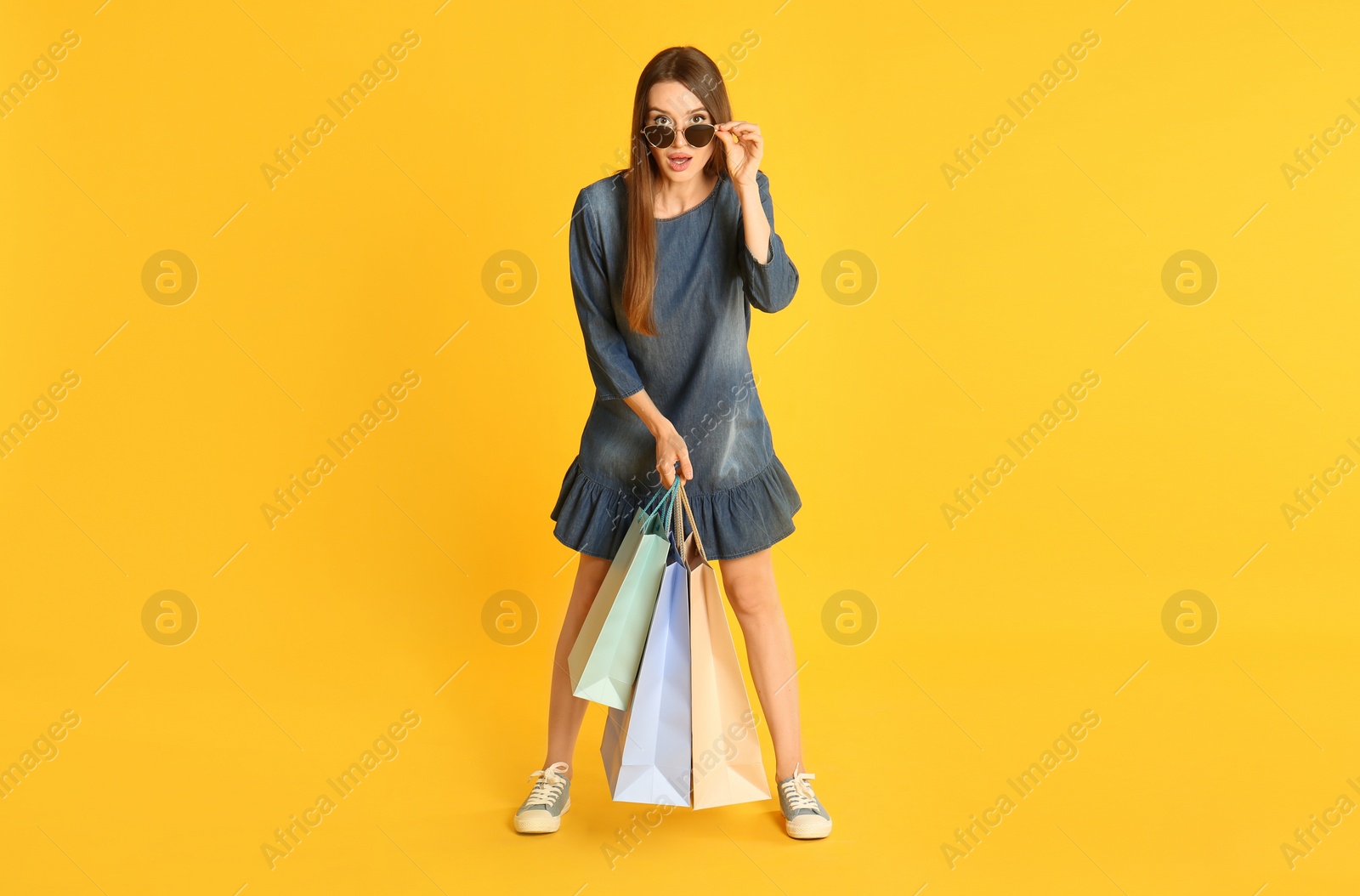 Photo of Beautiful young woman with paper shopping bags on yellow background