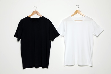 Photo of Hangers with blank t-shirts on white background. Mock up for design