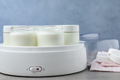 Modern yogurt maker with full jars on grey table, closeup