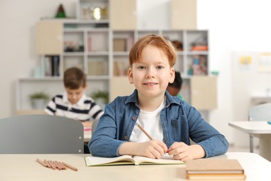 Portrait of smiling little boy studying in classroom at school. Space for text