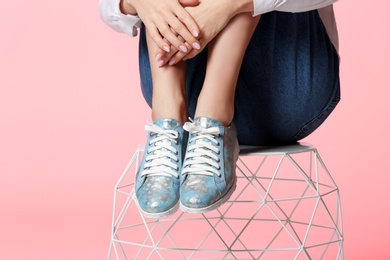 Woman in stylish shoes on stool against color background, closeup