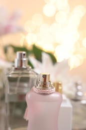 Bottles of perfume against beautiful lily flowers and blurred lights, closeup. Space for text