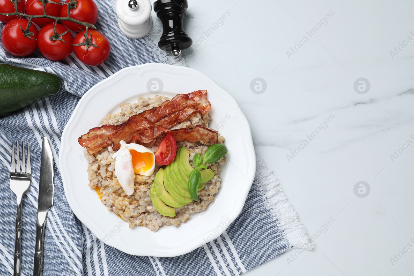 Photo of Delicious boiled oatmeal with egg, bacon, tomato and avocado served on white marble table, flat lay. Space for text