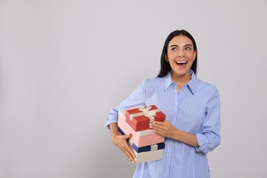 Photo of Emotional young woman holding gift boxes on light grey background, space for text