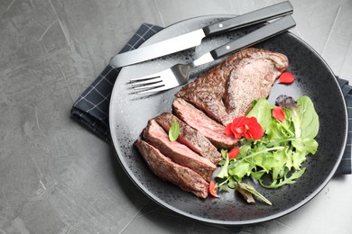 Photo of Delicious grilled beef meat served with greens on grey table. Space for text