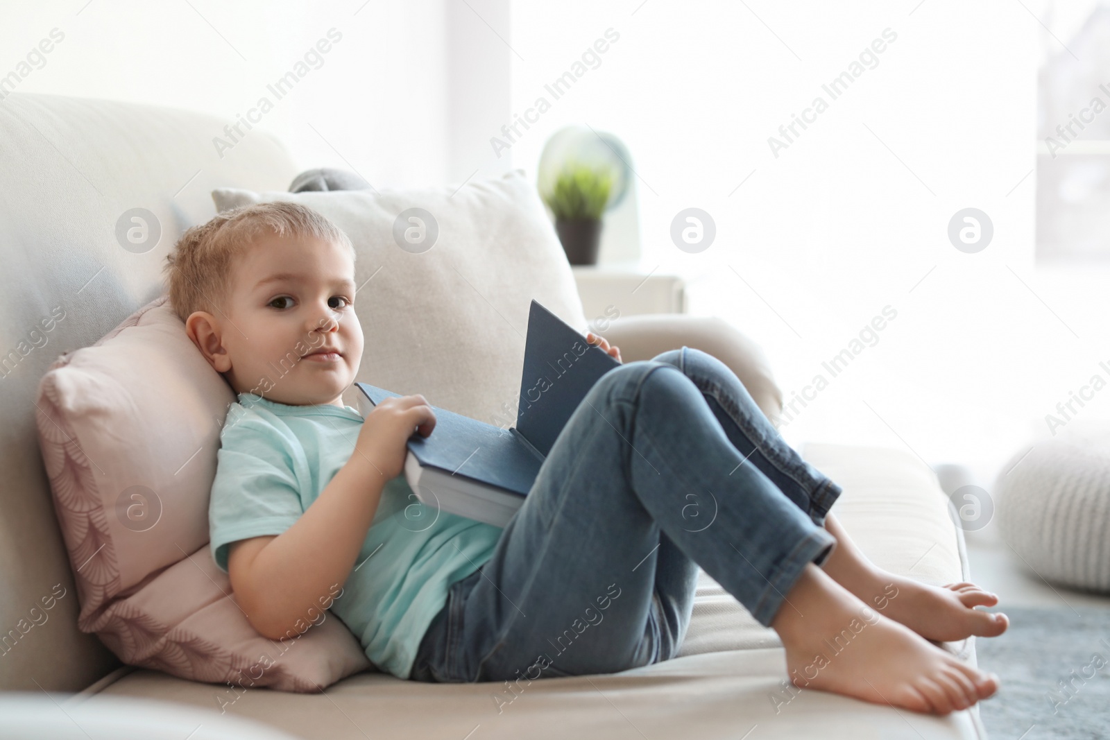 Photo of Cute child reading book on sofa indoors