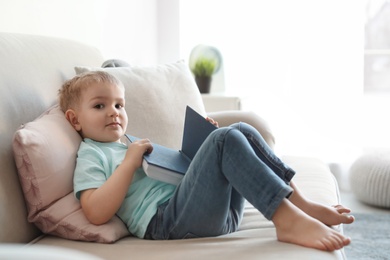 Photo of Cute child reading book on sofa indoors