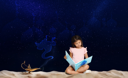 Image of Cute little girl reading magic book and Aladdin magic lamp on sand at night