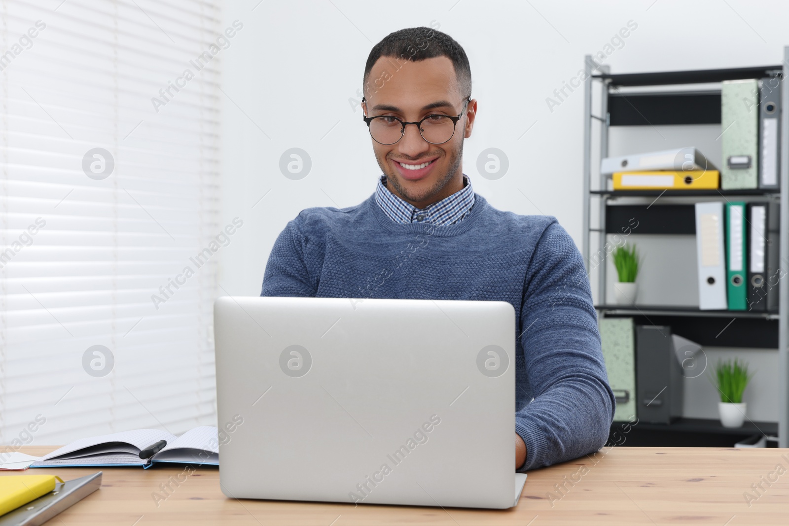 Photo of Happy young intern working with laptop at table in modern office