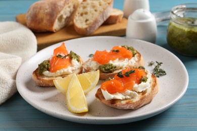 Photo of Delicious bruschettas with cream cheese, salmon and pesto sauce on light blue wooden table, closeup