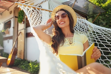 Young woman with book resting in hammock near motorhome outdoors on sunny day