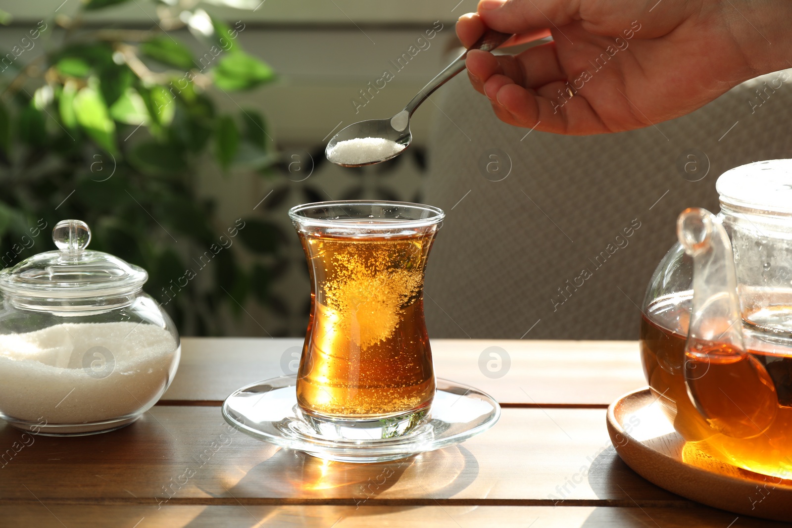 Photo of Woman adding sugar into aromatic tea at wooden table indoors, closeup