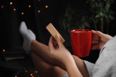 Woman with wafer and coffee on dark background, closeup. Early breakfast