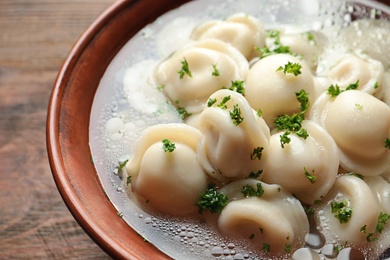 Bowl of tasty dumplings in broth on table, closeup