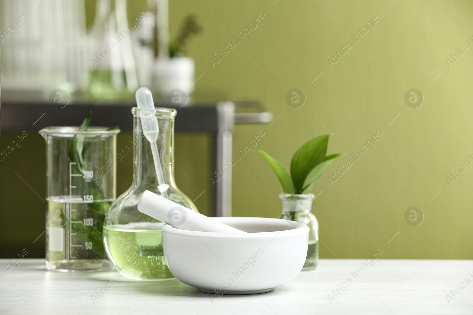 Photo of Mortar with pestle and natural ingredients on white table in cosmetic laboratory