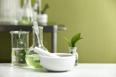 Photo of Mortar with pestle and natural ingredients on white table in cosmetic laboratory