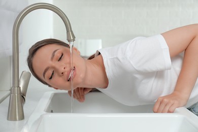 Photo of Woman drinking tap water over sink in kitchen