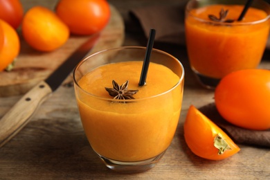 Photo of Tasty persimmon smoothie with anise and straw on wooden table, closeup