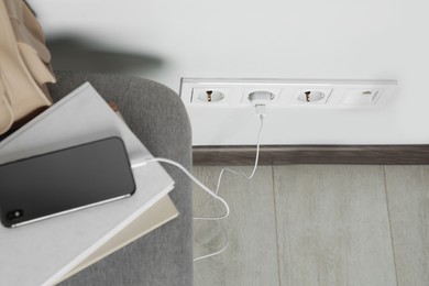 Photo of Electric power outlet sockets with charger on white wall, above view