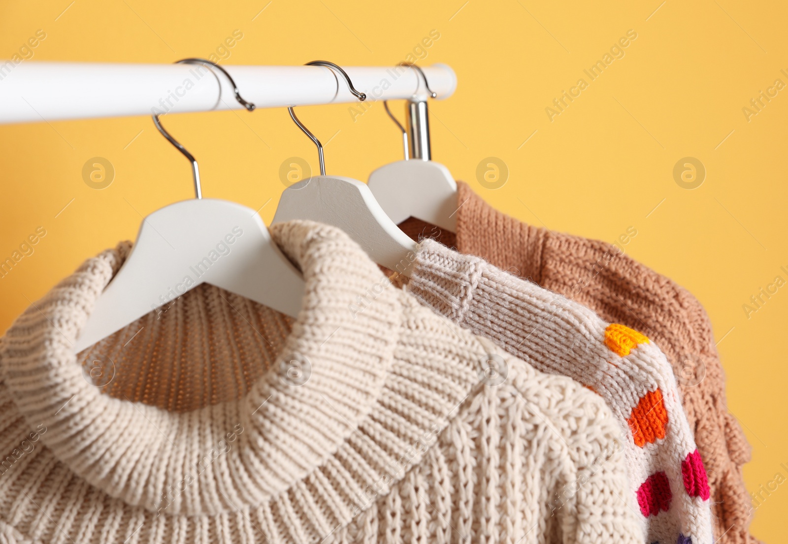 Photo of Collection of warm sweaters hanging on rack against color background, closeup