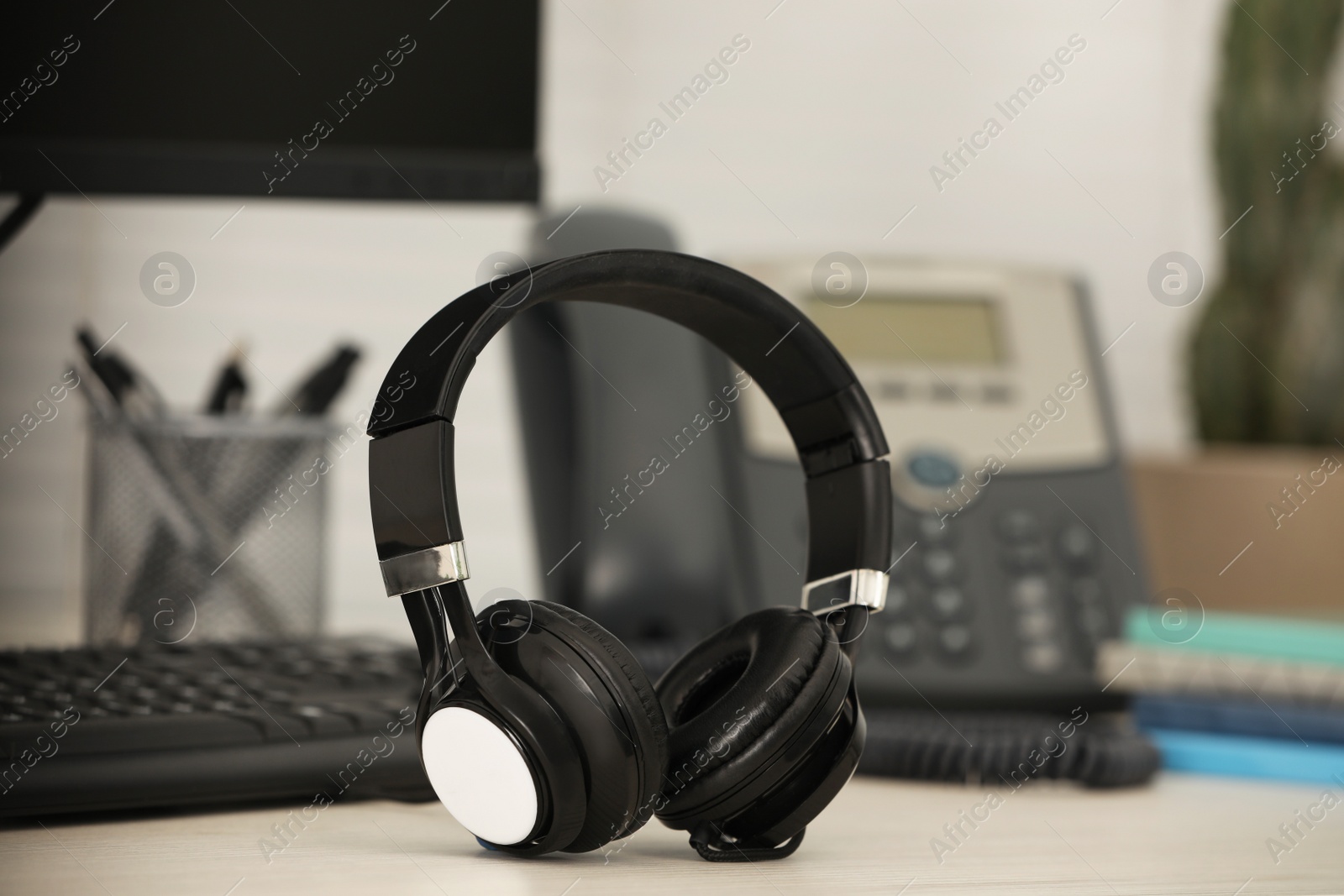 Photo of Modern headphones, desktop telephone and computer on table indoors