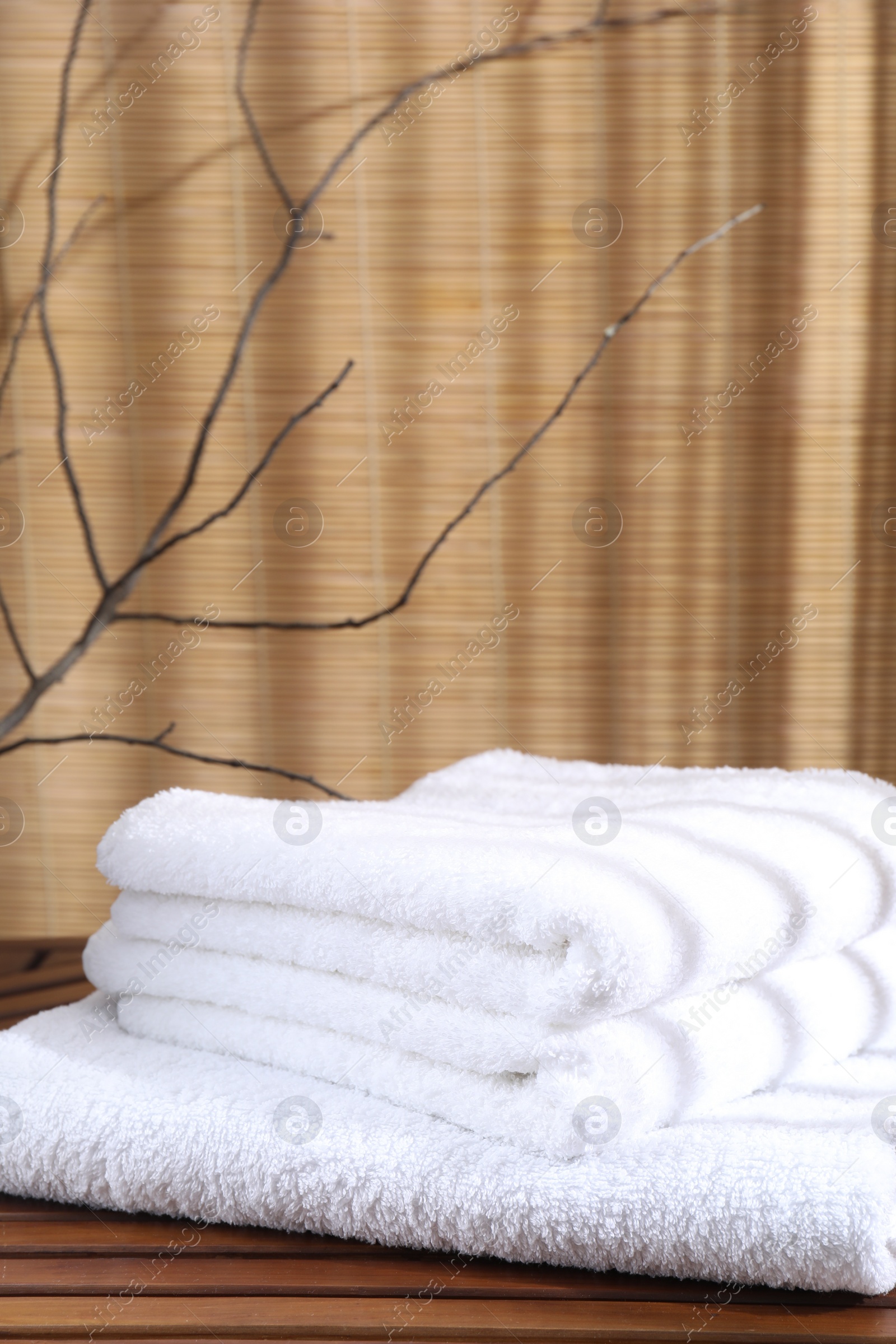 Photo of Stacked soft towels on wooden table and tree branches indoors