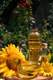 Photo of Bottles and bowl with sunflower oil on wooden table outdoors