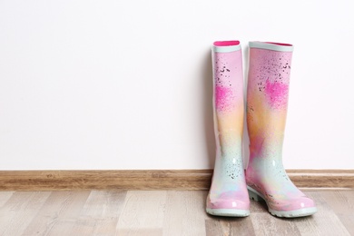 Photo of Pair of gumboots on wooden floor against white wall. Female shoes